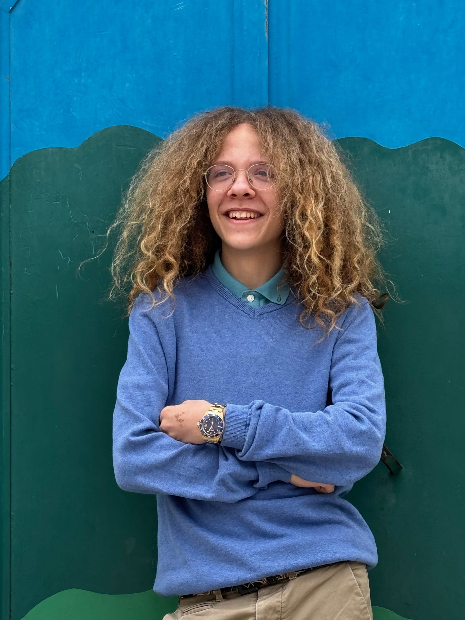 Uczeń stojący z założonymi rękami na tle niebiesko-zielonej ściany.