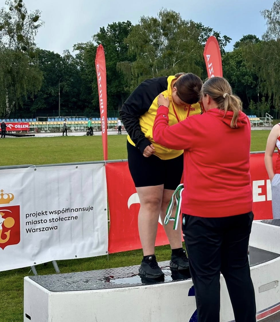 Uczennica odbiera medal, stojąc na podium podczas zawodów lekkoatletycznych w Warszawie.