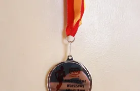 Medal zdobyty przez uczennicę podczas Mistrzostw Warszawy Młodzików, zawieszony na czerwono-żółtej wstążce.