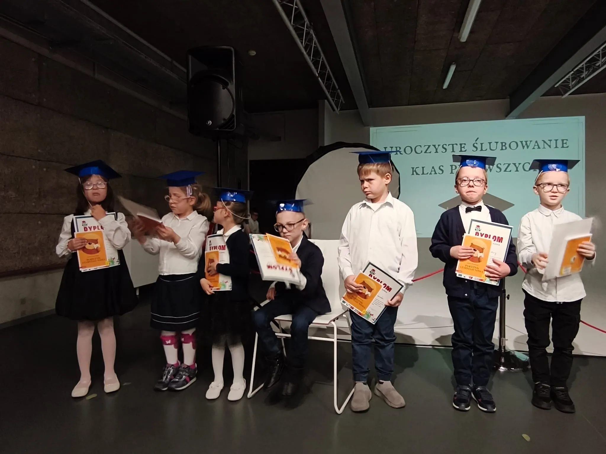 Pierwszoklasiści podczas uroczystego ślubowania z dyplomami w rękach.