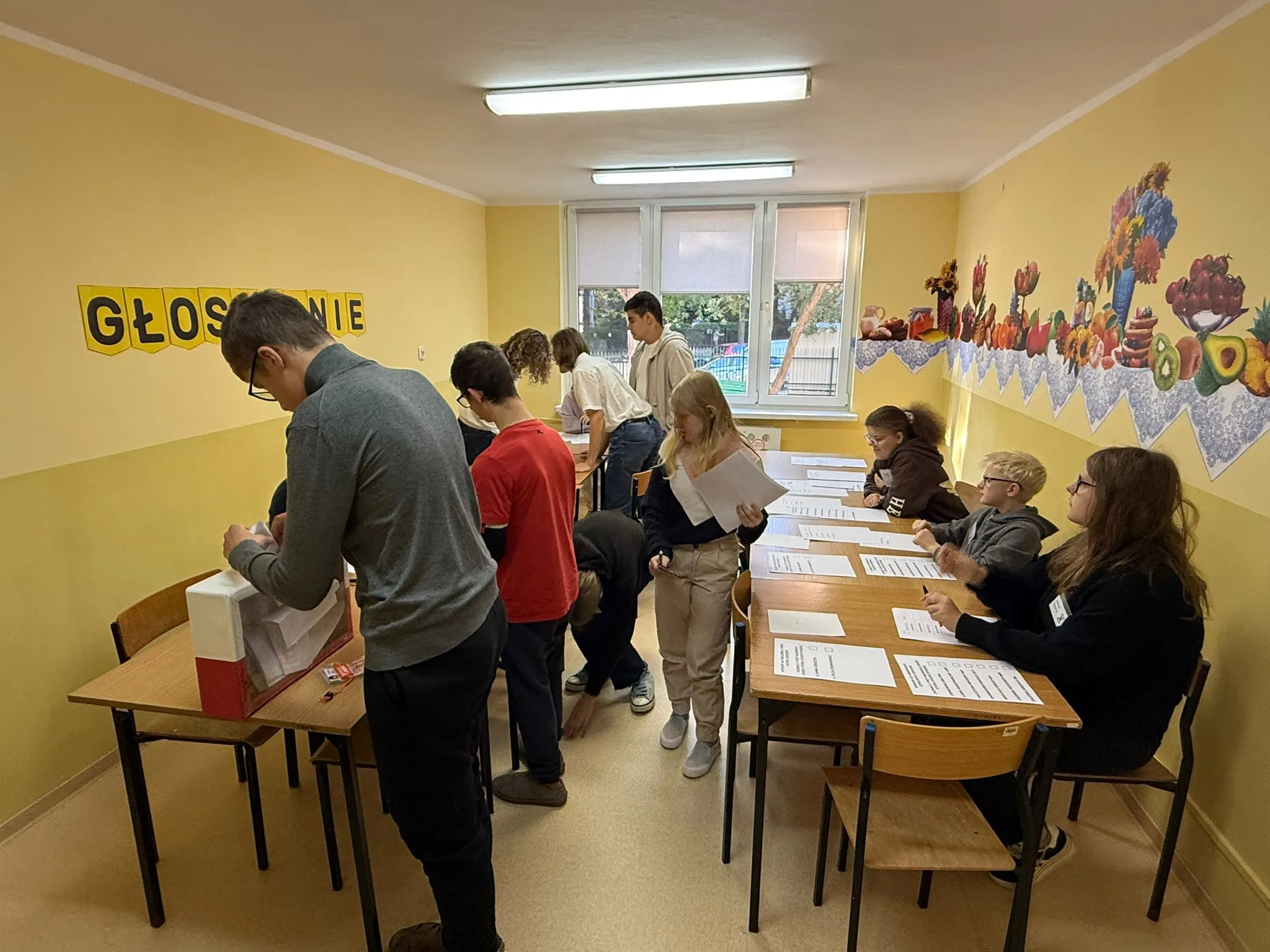 Grupa uczniów bierze udział w głosowaniu w szkolnej sali.