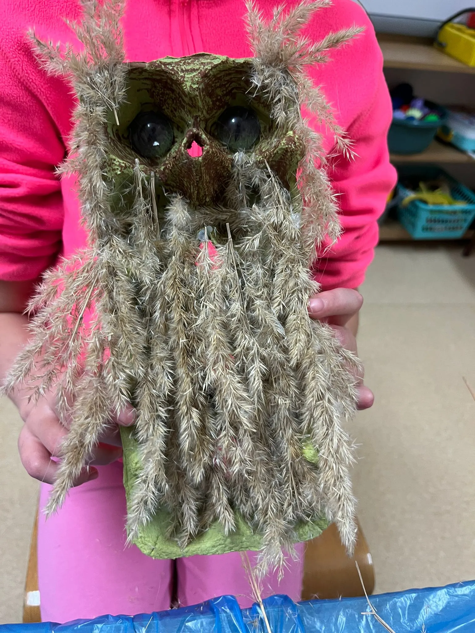 Uczeń trzyma własnoręcznie wykonaną figurkę sowy z zielonego kartonu i suszonych traw. Praca powstała podczas zajęć arteterapii rozwijających kreatywność i wyobraźnię.
