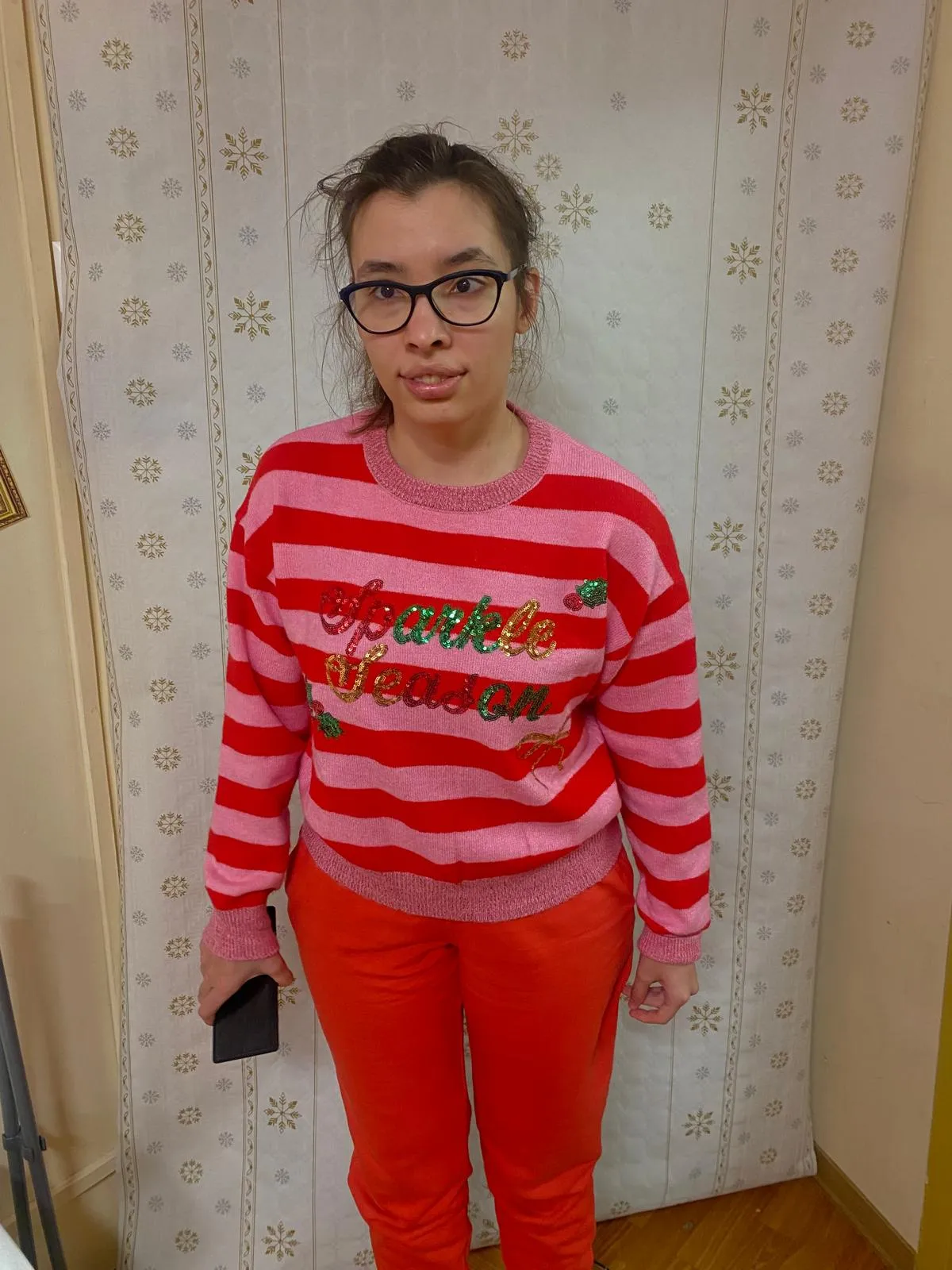 Na zdjęciu widoczna jest uśmiechęnięta dziewczyna w kasku na głowie. Ubrana jest w sweter w czerwono-różowe poziome paski, na którym widenieje wielokolorowy brokatowy napis "Sparkles Season"