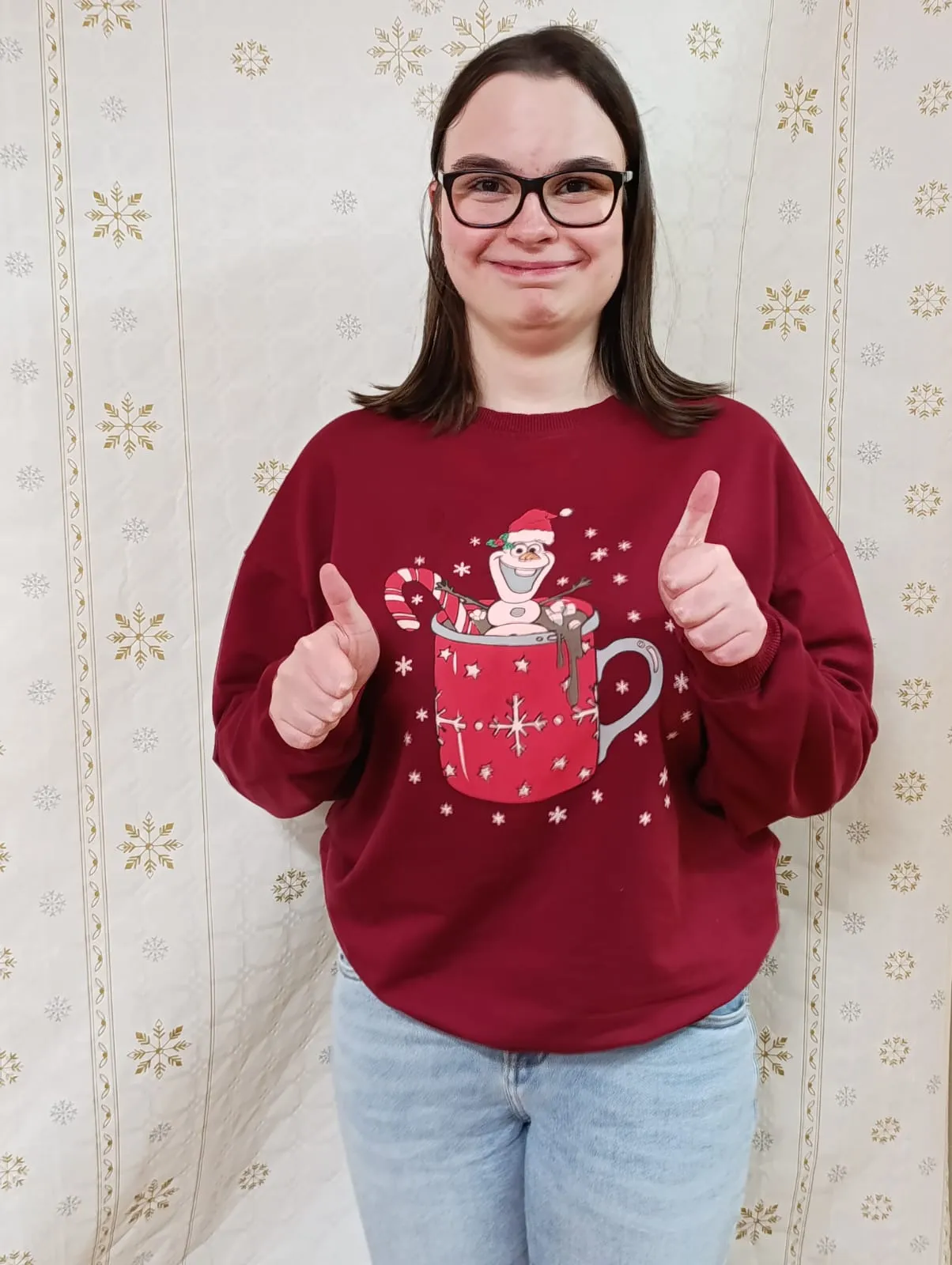 Na zdjęciu widoczna jest uśmiechęnięta dziewczyna w kasku na głowie. Ubrana jest w czerwony sweter z czerwonym kubkiem gorącej czekolady, w którym Bpływa bałwanek z filmu Kraina Lodu - Olaf wraz ze świątecznymi słodyczami